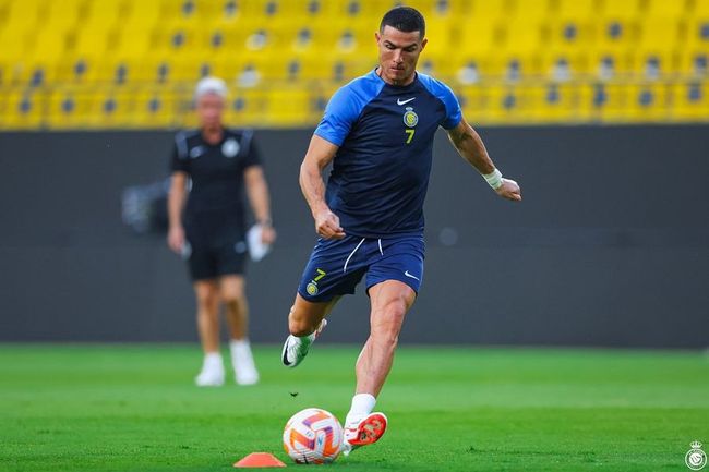 Cristiano Ronaldo, wearing a blue number 7 kit, kicks a soccer ball on the pitch with another player in the background.