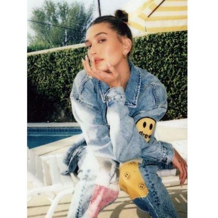 A woman in a patched denim jacket by a pool, looking pensive.