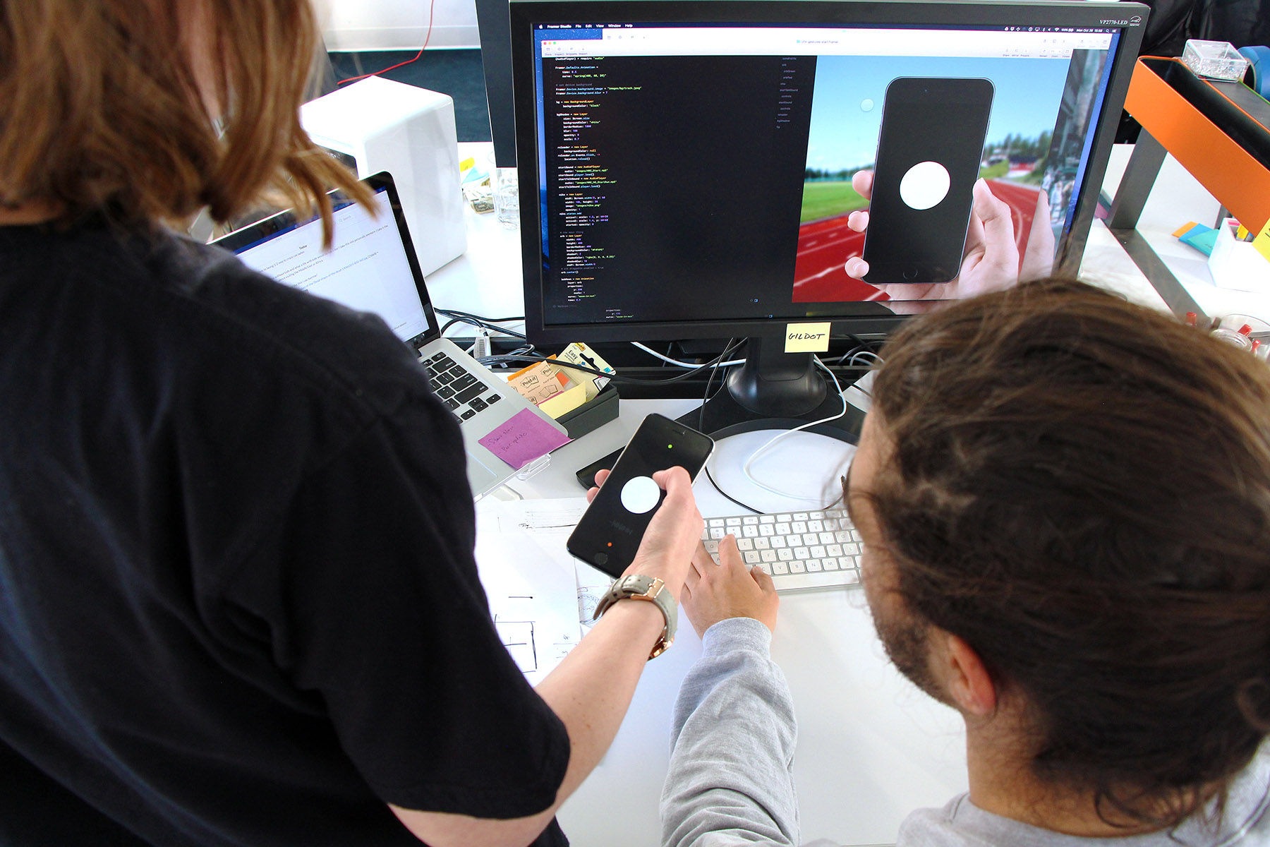Two people experimenting with a phone prototype, in front of a computer display
