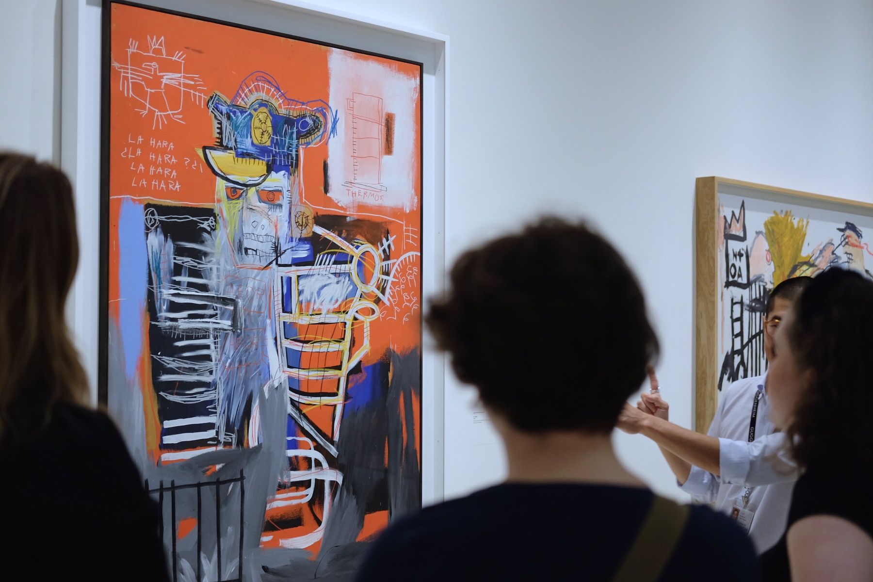 A museum guide explaining a Basquiat painting to people.