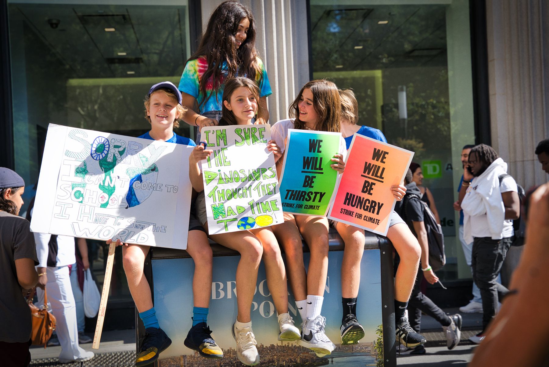 Four kids sitting on garbage bins and holding Climate Strike posters