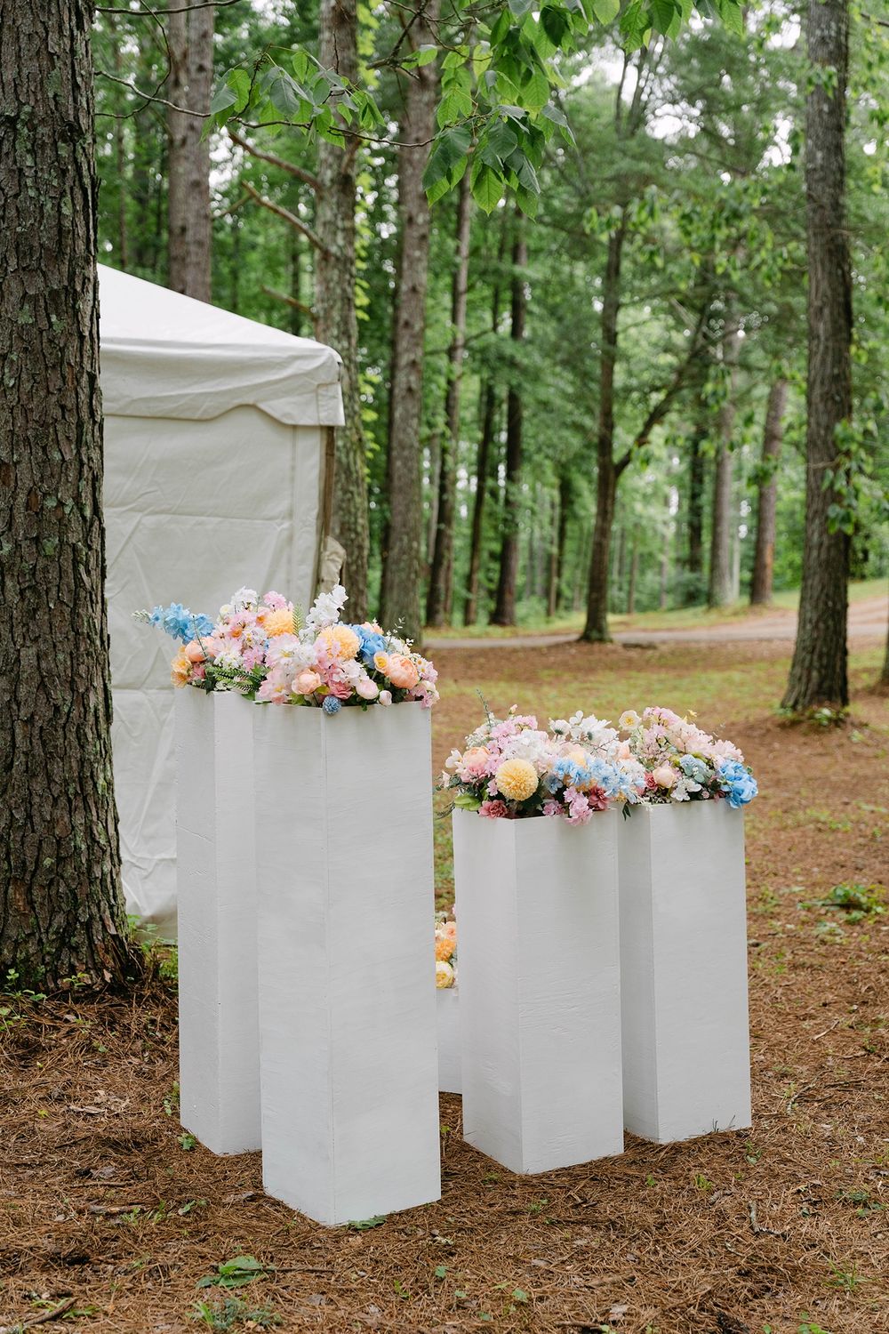 pastel wedding florals arranged on white pedestals in a pine forest