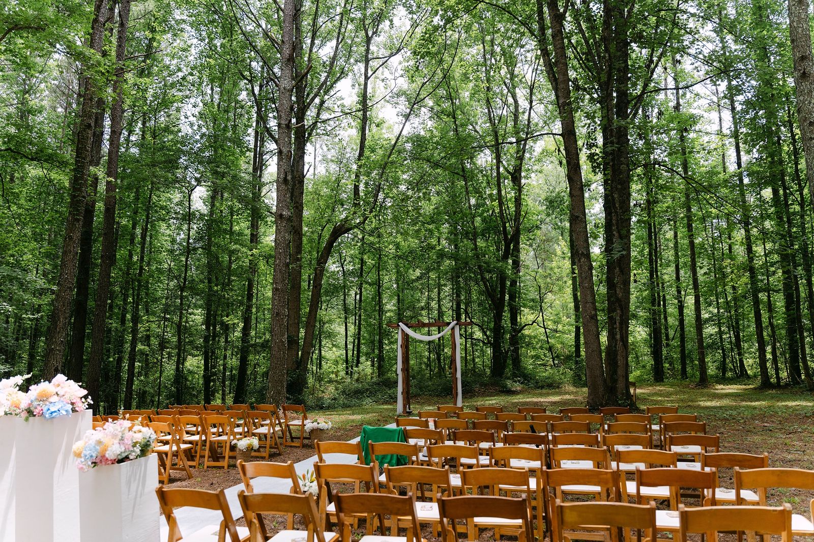 forest wedding ceremony site with wooden arbor and white aisle among tall pine trees