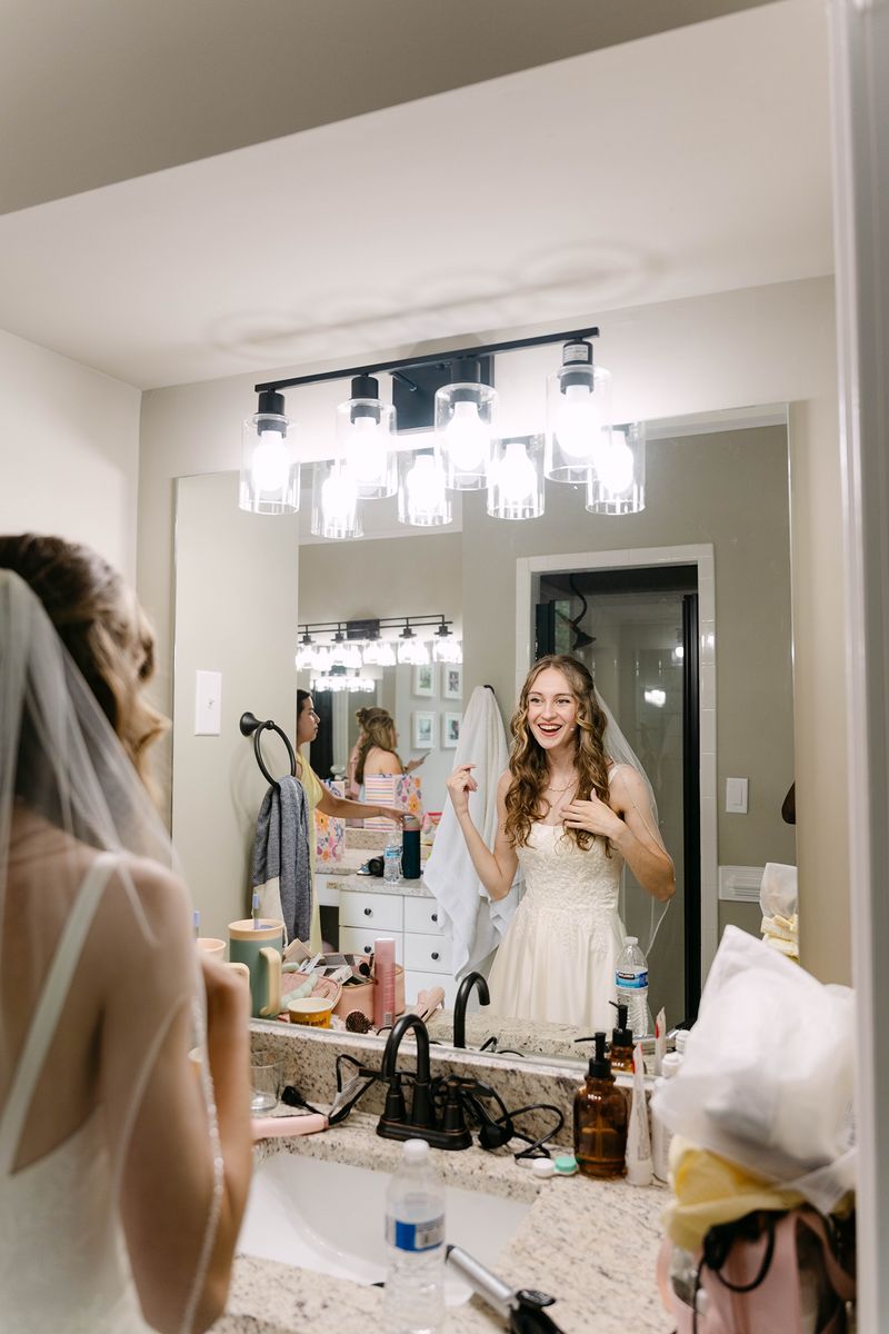 bride smiling at her reflection with her bridesmaids beside her