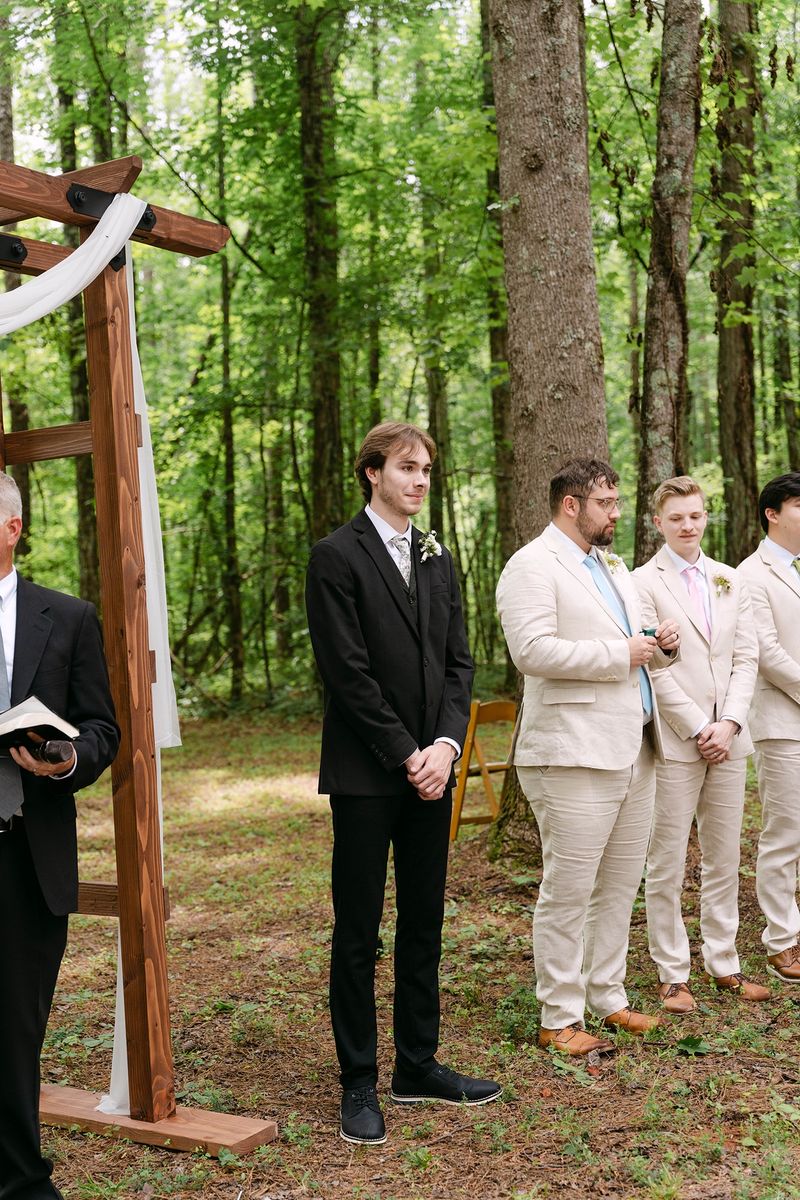 groom waiting at the wooden arbor with the officiant and groomsmen