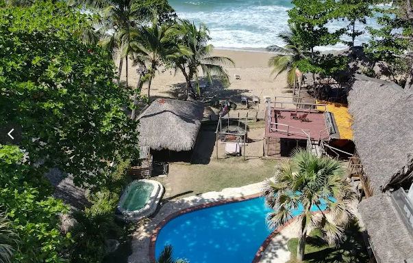 "Aerial view of a pool with jacuzzi, surrounded by palm trees and tropical-style cabanas facing the beach, ideal for transfers with Taxi Dominicana in Punta Cana" 