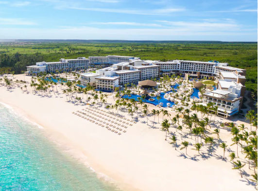 Bar de piscina con techo de palapa en un resort de lujo, con gran piscina azul y palmeras