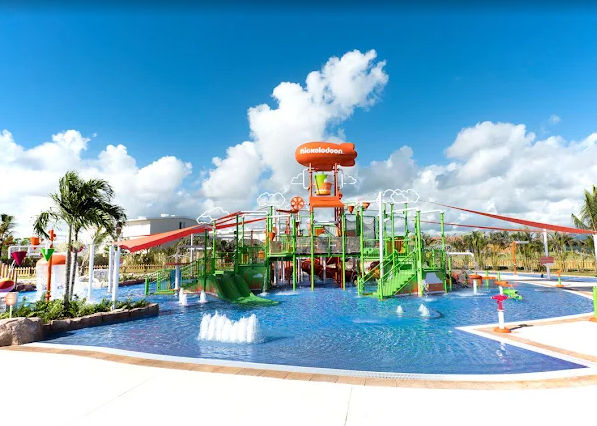 "Aqua Nick water park with colorful green slides, a shallow pool, and the iconic orange Nickelodeon blimp at Nickelodeon Hotels and Resorts Punta Cana."
