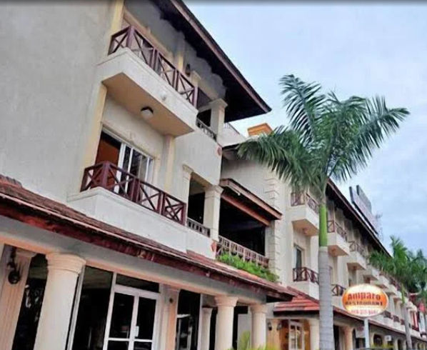"Exterior facade of the hotel with wooden balconies, columns and tropical palm trees at the entrance, highlighting the sign of the Amparo restaurant."