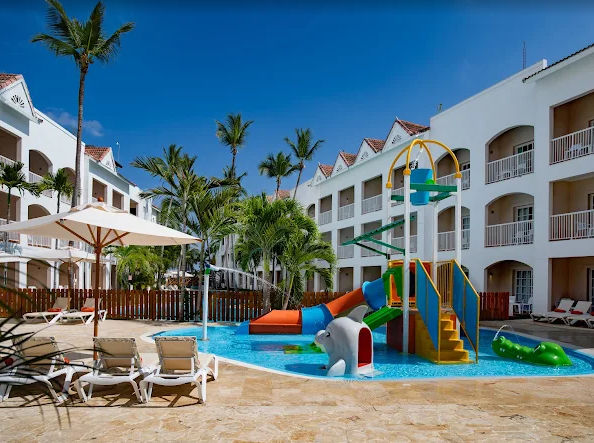 Interior courtyard of a residential complex with green lawn, a rectangular swimming pool, a circular jacuzzi in the foreground and white Mediterranean-style apartment buildings around it.