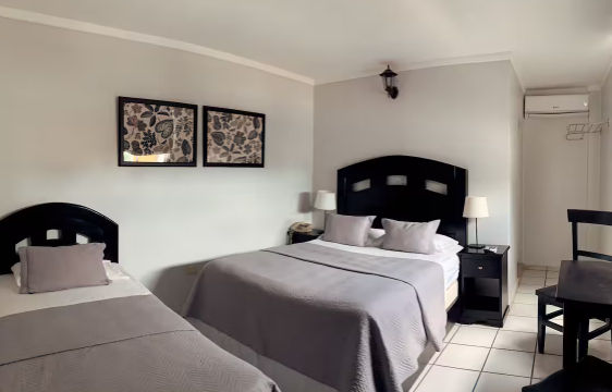 Fachada frontal de un hotel de varios niveles con tonos marrones y blancos, con señalización roja distintiva en la parte superior y área de recepción abierta en la planta baja