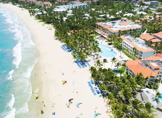 Vista aérea de playa paradisíaca en Cabarete con resort de lujo, palmeras y kitesurfistas; reserva tu transporte seguro con Taxi Dominicana para llegar cómodamente.