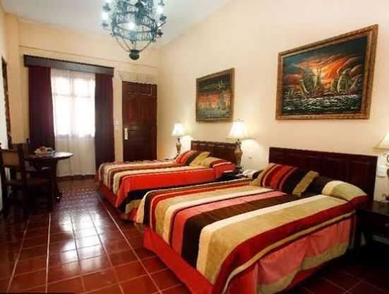 Patio interior de un hotel con mesas y sillas de hierro, rodeado por un edificio colonial y una pared de piedra histórica con vegetación