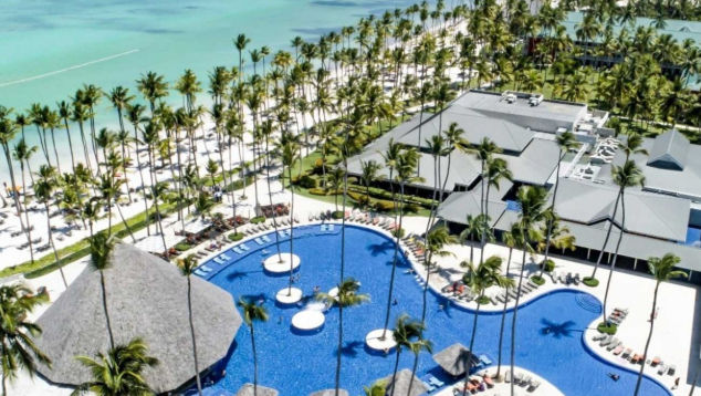 Vista aérea de un complejo hotelero con una gran piscina azul, edificios con techos de tejas rojas y jardines tropicales