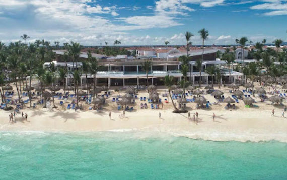 Vista aérea de un complejo hotelero con una gran piscina azul, edificios con techos de tejas rojas y jardines tropicales