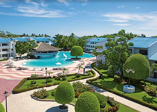 "Panoramic view of a tropical resort with a central pool, blue-roofed buildings, and meticulously maintained gardens."