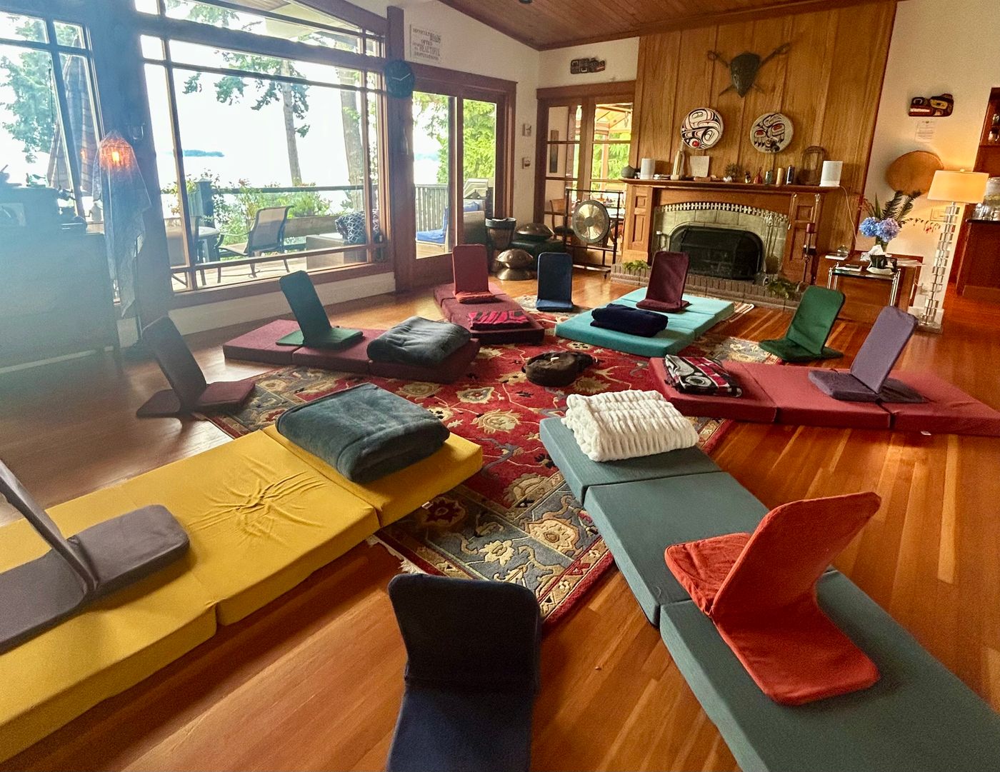 A circle of mats and floor chairs laid out in our living room, fireplace on one side and the water through the windows