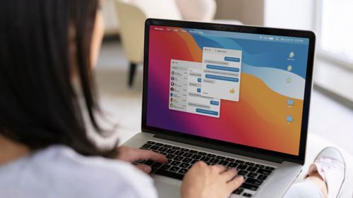 A woman operates a laptop with a vibrant screen showing steps for copying and pasting on a Mac computer.