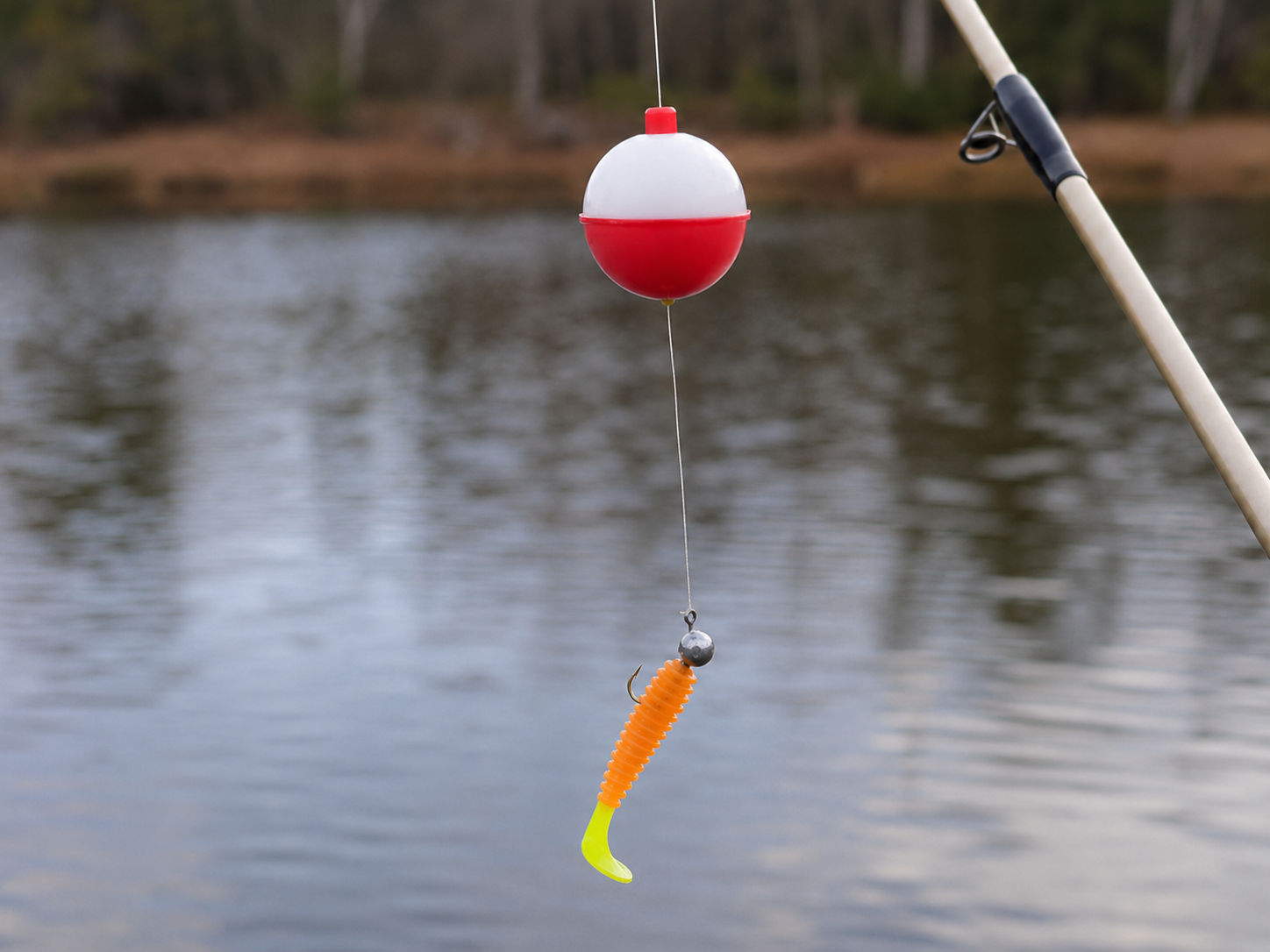 Round red and white fishing float rigged above a plain jig head and soft plastic for crappie