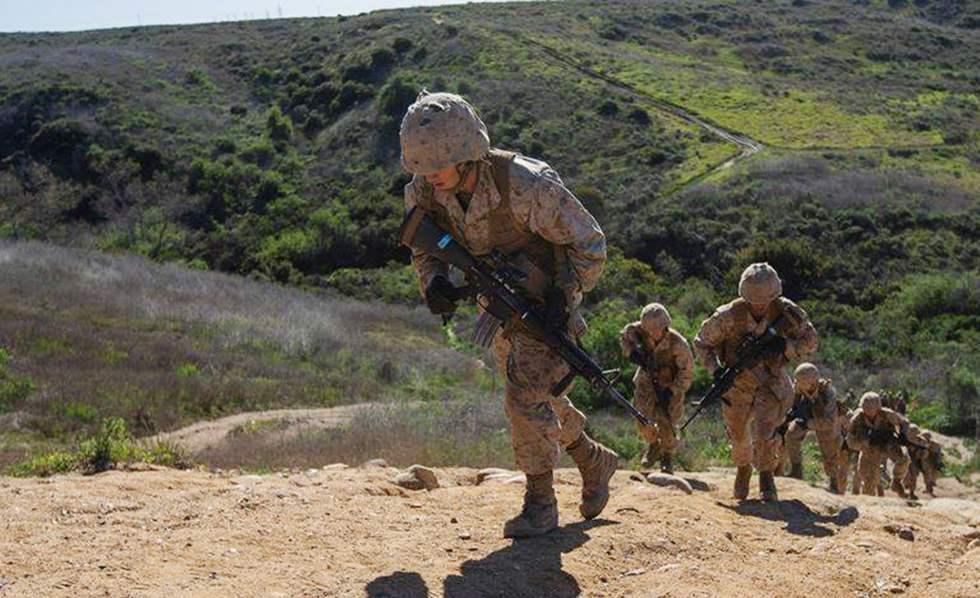 Marines moving uphill in file across the scrub and open country of Camp Pendleton.