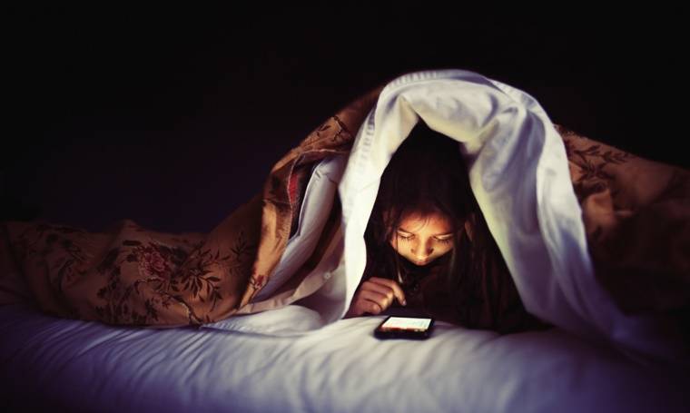 a girl looking at a phone under the bed covers