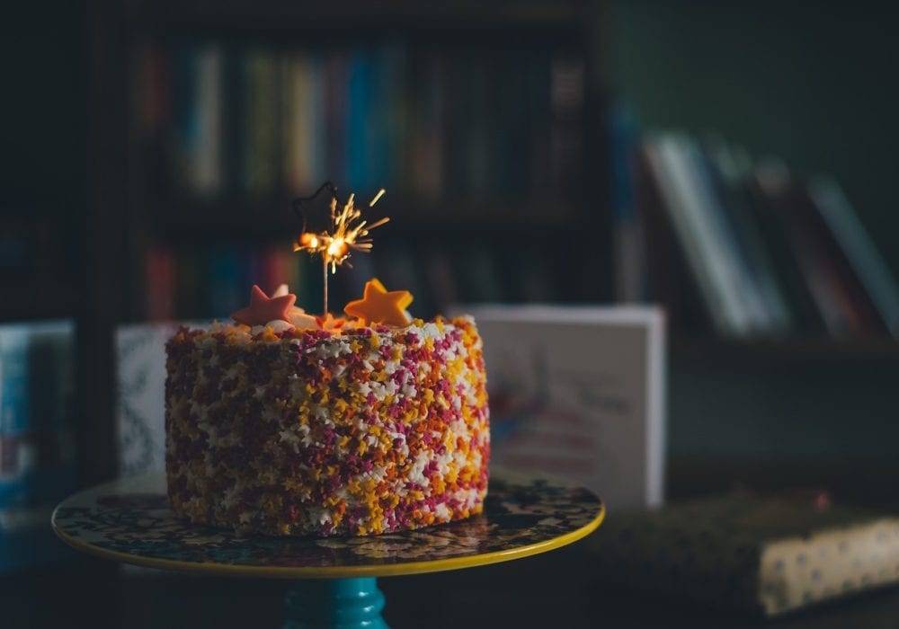 a colorful birthday cake covered with sprinkles and one candle