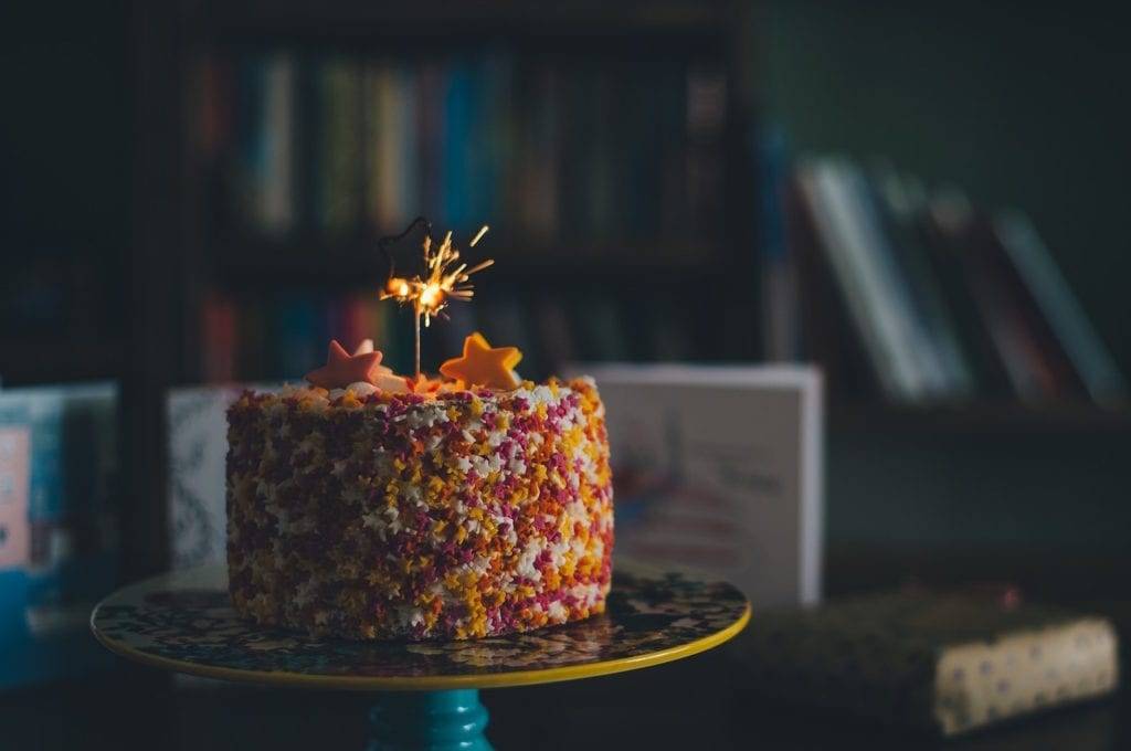 a colorful birthday cake covered with sprinkles and one candle
