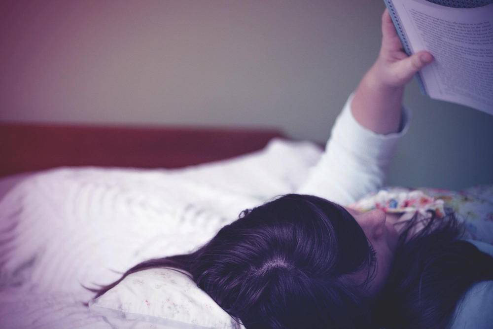 a woman resting in bed reading a book