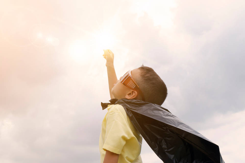 little boy with a superhero cape on and his fist pointed to the sky