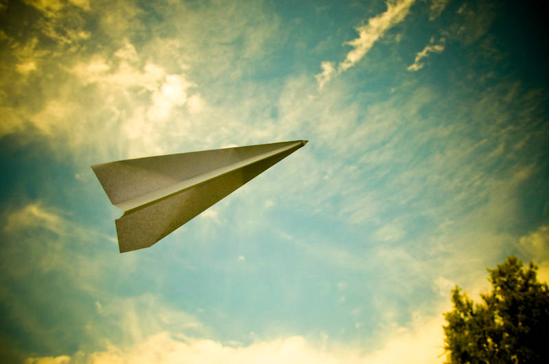 paper airplane flying with blue sky overhead