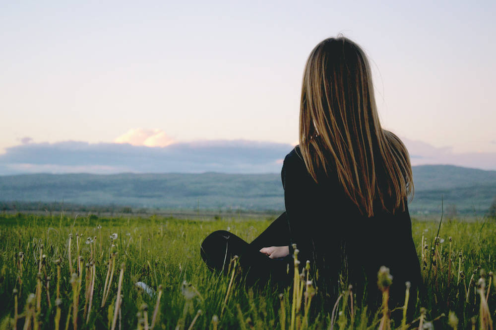 a woman sitting in a grass field looking outward