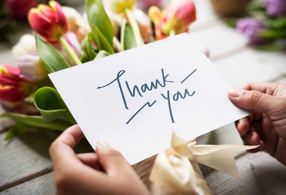 hand holding a thank you card and bouquet of flowers