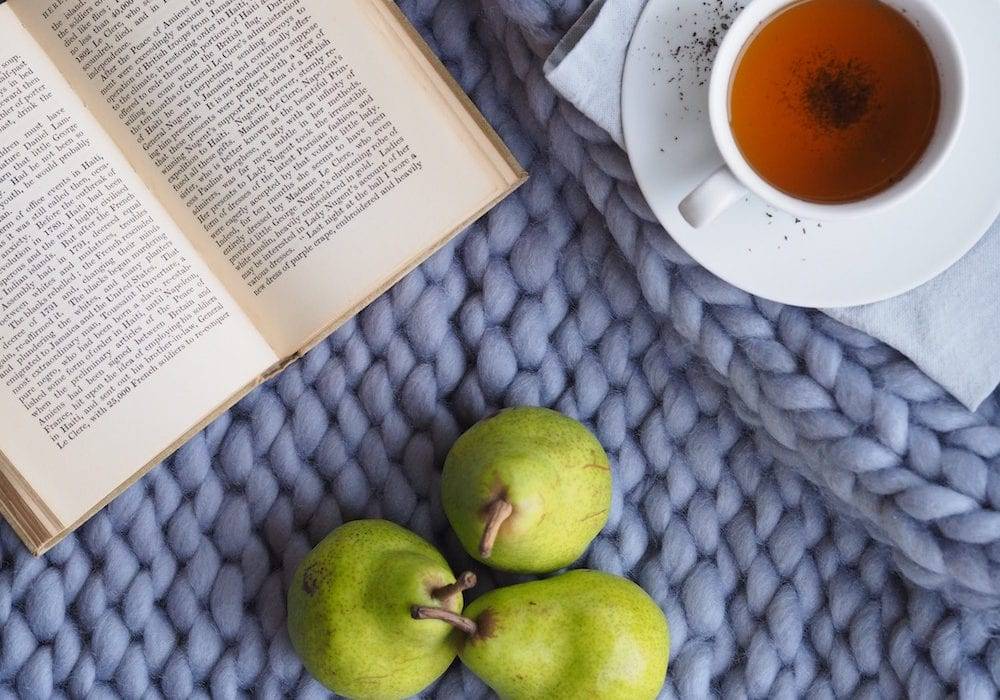 A book, cup of tea, and pears sitting on a placemat