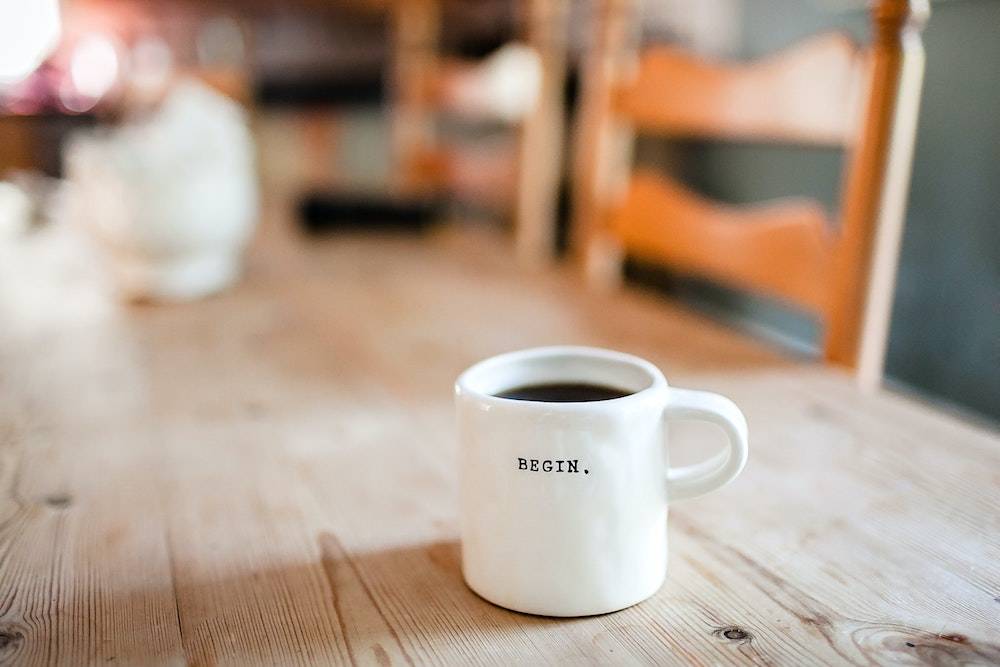 coffee mug on a wood table that says "begin"