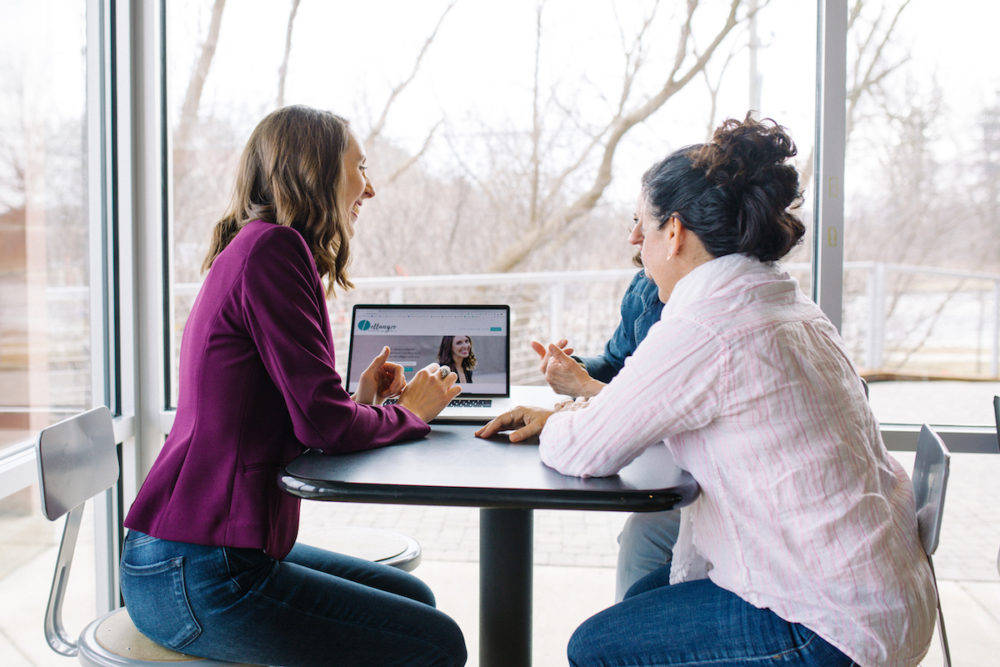 Janelle sitting at a high-top table with some clients looking at a computer laptop together