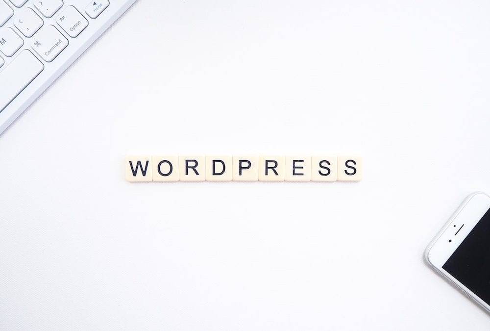 best plugins for wordpress - tiles on a desk spelling out wordpress with computer keyboard and phone nearby