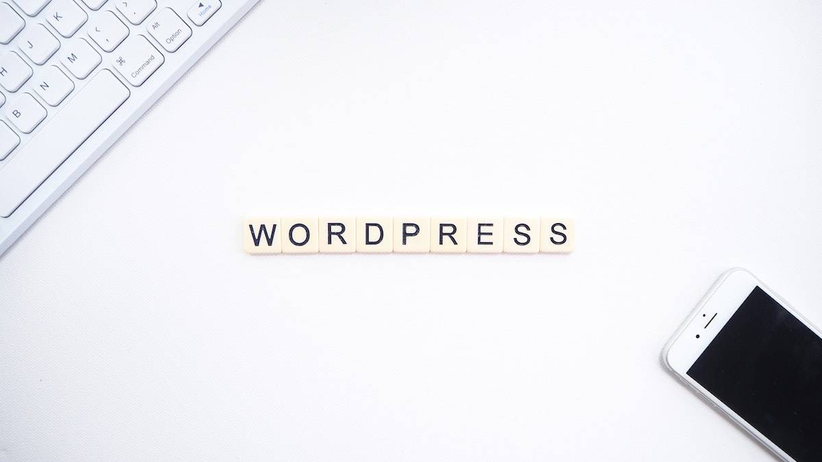 best plugins for WordPress - tiles on a desk spelling out wordpress with computer keyboard and phone nearby