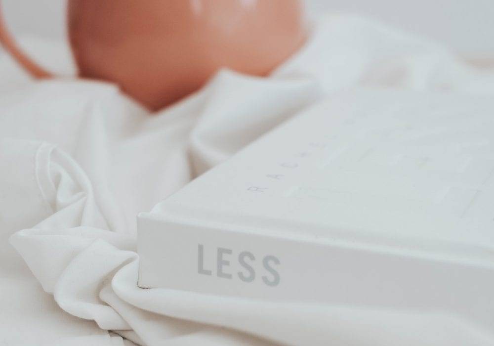 What Do You Need To Be Happy? a white book laying in the bed sheets with the word "LESS" on the spine