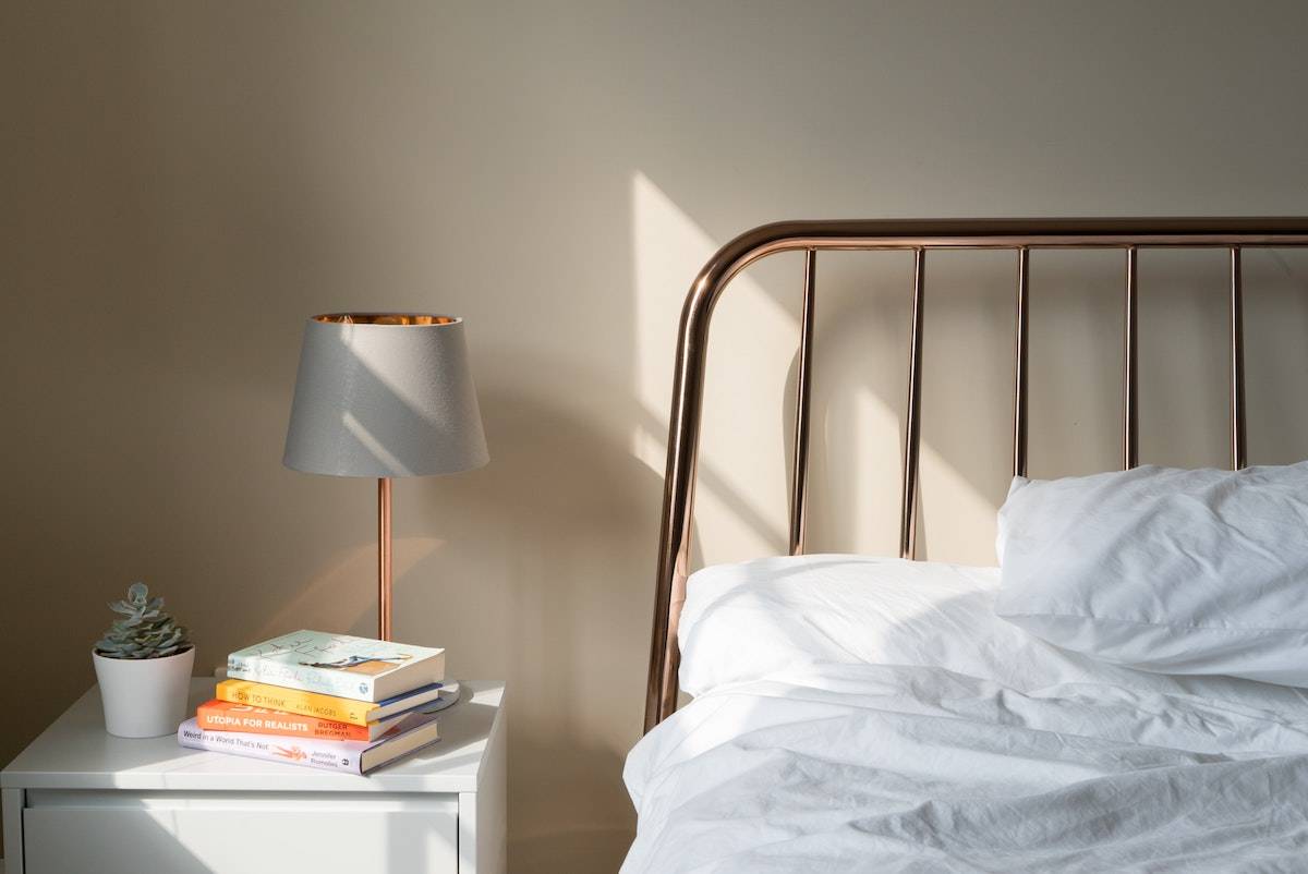 How to get the best sleep at night: a relaxing bed, nightstand and lamp with morning light pouring in