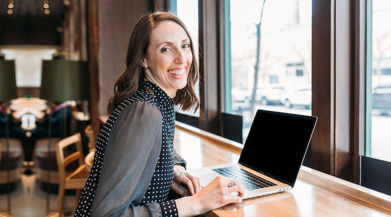 Ann Arbor Michigan web designer Janelle Reichman sitting with her laptop at a coffee shop smiling