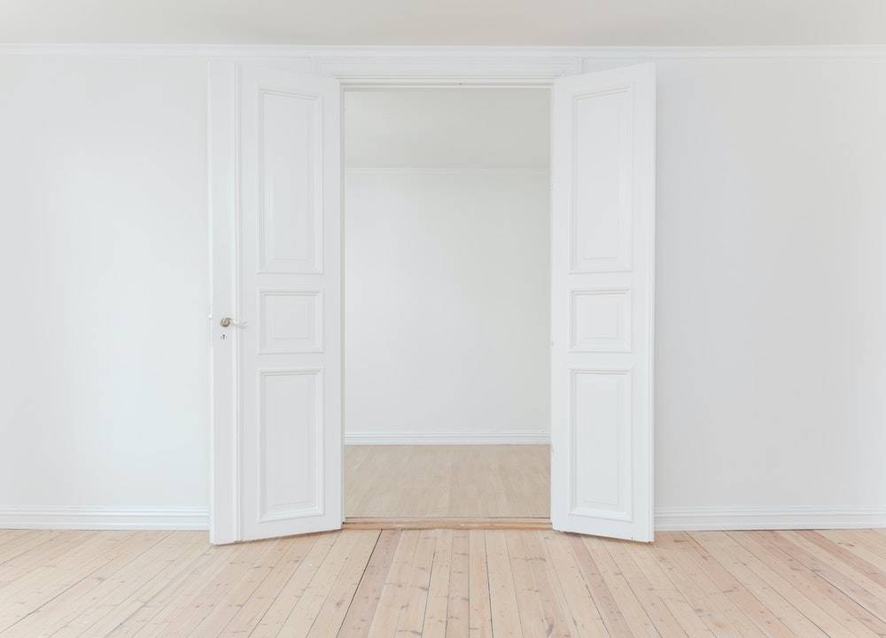 Begin living a minimalist lifestyle - two white doors opening up to an empty white room