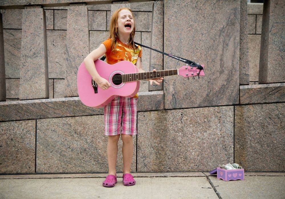 little girl singing and playing guitar on the street for money