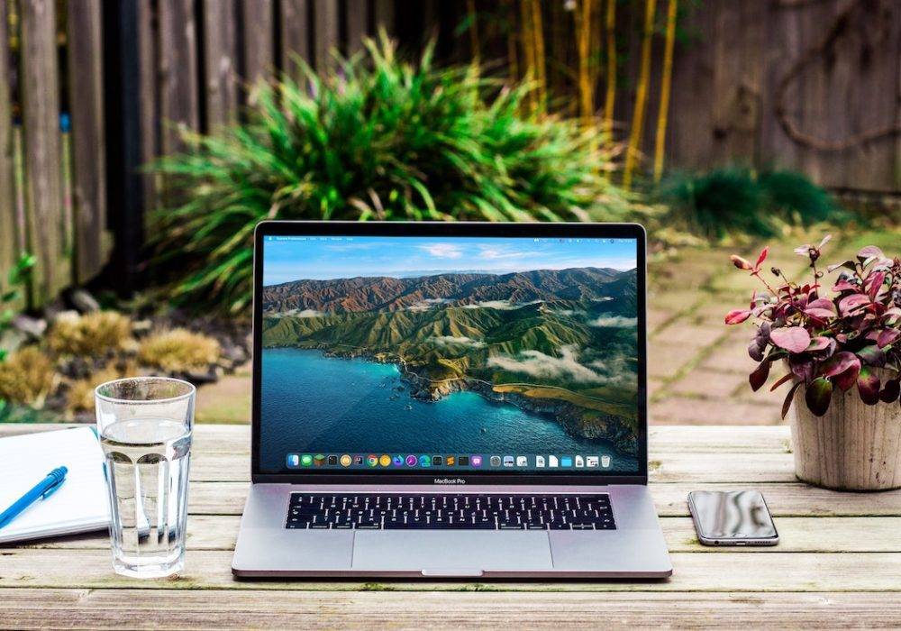 laptop on an outdoor table with flowers, glass of water, sunny day