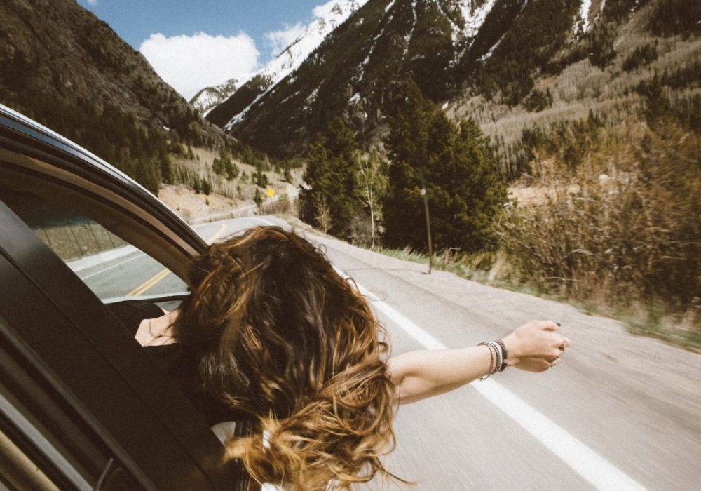 moments of euphoria - a woman with her hand out the car window riding in the mountains