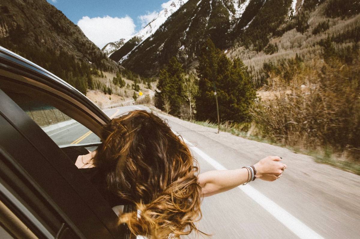 moments of euphoria - a woman with her hand out the car window riding in the mountains