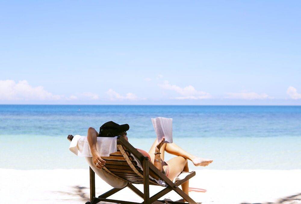 a woman resting in a chair on the beach reading a book