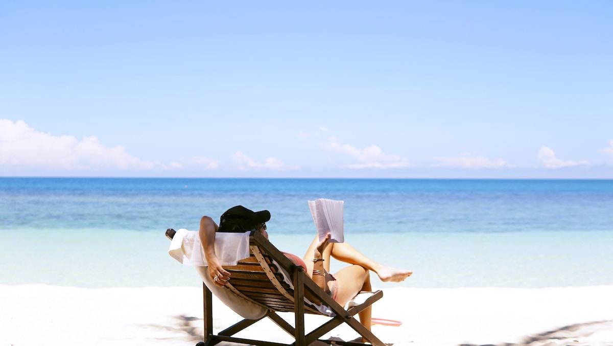 a woman resting in a chair on the beach reading a book