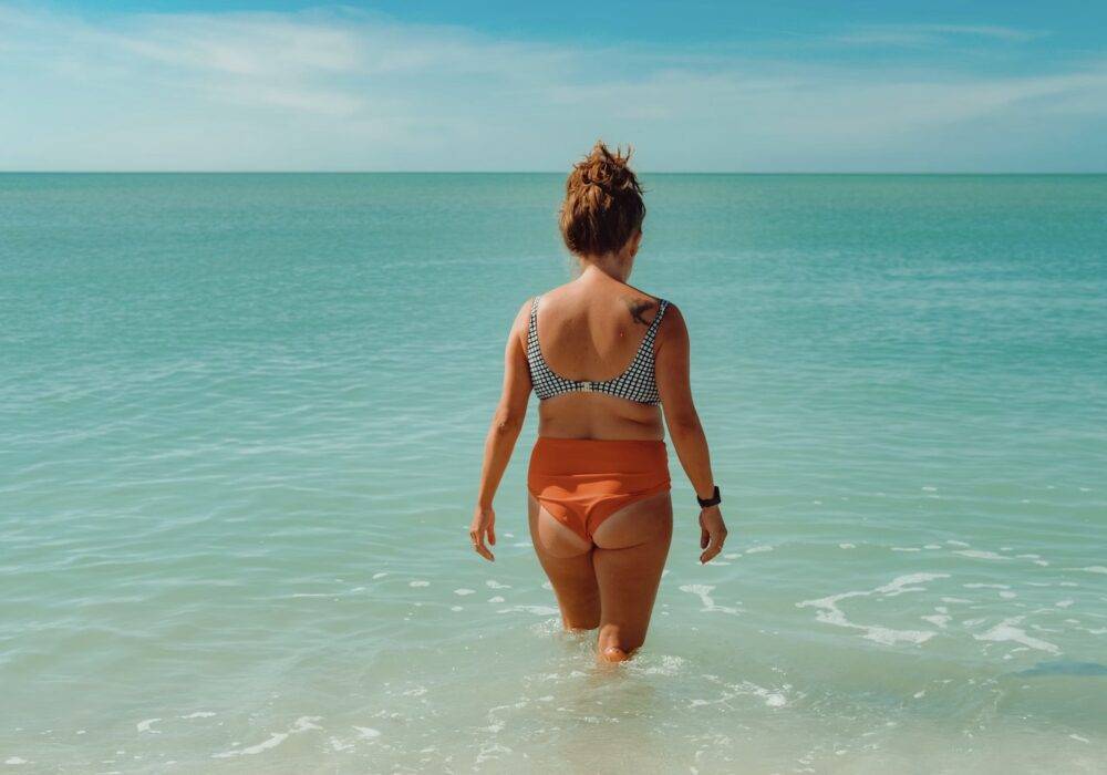 a woman walking into the ocean in her bathing suit