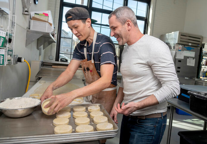WEEKEND WARRIORS: Knead Doughnuts co-owner Adam Lastrina, right, and Bryan Tsai, production supervisor, prepare doughnuts in March. While the bakery has three locations in Rhode Island, only one remains open, serving takeout orders on the weekends only. / PBN FILE PHOTO/MICHAEL SALERNO WEEKEND WARRIORS: Knead Doughnuts co-owner Adam Lastrina, right, and Bryan Tsai, production supervisor, prepare doughnuts in March. While the bakery has three locations in Rhode Island, only one remains open, serving takeout orders on the weekends only. / PBN FILE PHOTO/MICHAEL SALERNO