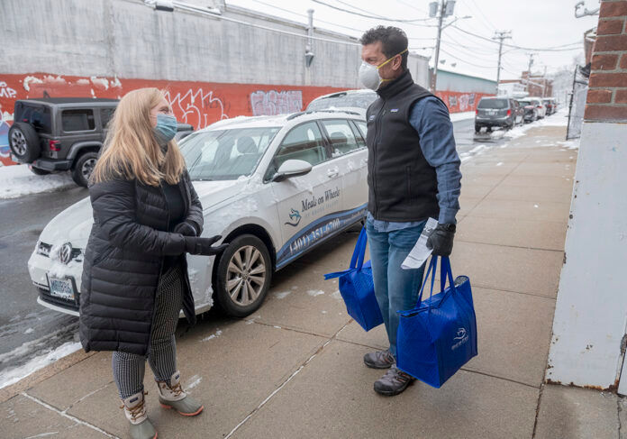 LOADING UP: Meg Grady, executive director for Meals on Wheels of Rhode Island, and volunteer Ted Fischer, CEO of Ageless Innovation, help load food into vehicles for some deliveries. Grady said the organization’s home-delivery program saw a 7% increase in seniors served and a 9% increase in meals served in 2020 compared with 2019. / PBN PHOTO/MICHAEL SALERNO LOADING UP: Meg Grady, executive director for Meals on Wheels of Rhode Island, and volunteer Ted Fischer, CEO of Ageless Innovation, help load food into vehicles for some deliveries. Grady said the organization’s home-delivery program saw a 7% increase in seniors served and a 9% increase in meals served in 2020 compared with 2019. / PBN PHOTO/MICHAEL SALERNO